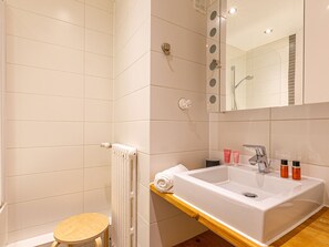 Ein modernes Badezimmer mit einem weißen Waschbecken, einem Spiegel und einem hölzernen Hocker.