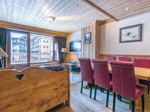 A wooden room with a bed, a dining table with red chairs, a TV on the wall, and a window with a view of buildings. - Elegant Apartment with Terrace, WiFi, Ski-In/Ski-Out in Val-d'Isère (Val-d'Isère)