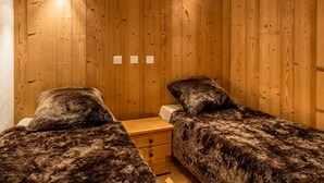 A room with wooden walls, two beds with dark, furry bedding, a wooden nightstand, and a ceiling light.