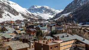 Un pueblo montañoso con edificios de madera tradicionales, un telesilla y cumbres nevadas al fondo.