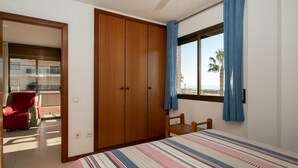 Una camera da letto con un letto grande, un armadio in legno, una finestra con tende blu e vista sulla spiaggia.