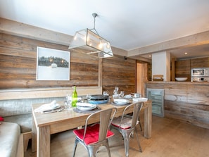 A dining area with a wooden table set for four, a chandelier, and a kitchen in the background.