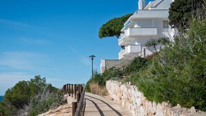 A coastal road leading to a white building with multiple balconies, surrounded by greenery and a clear blue sky. - Seafront Apartment with Terrace and Parking (Altafulla)