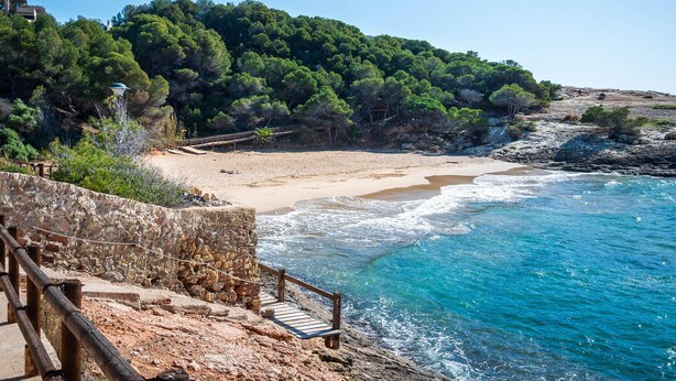 A coastal landscape with a sandy beach, rocky cliffs, and a wooden staircase leading down to the beach. - Seafront Apartment with Terrace and Parking (Altafulla)