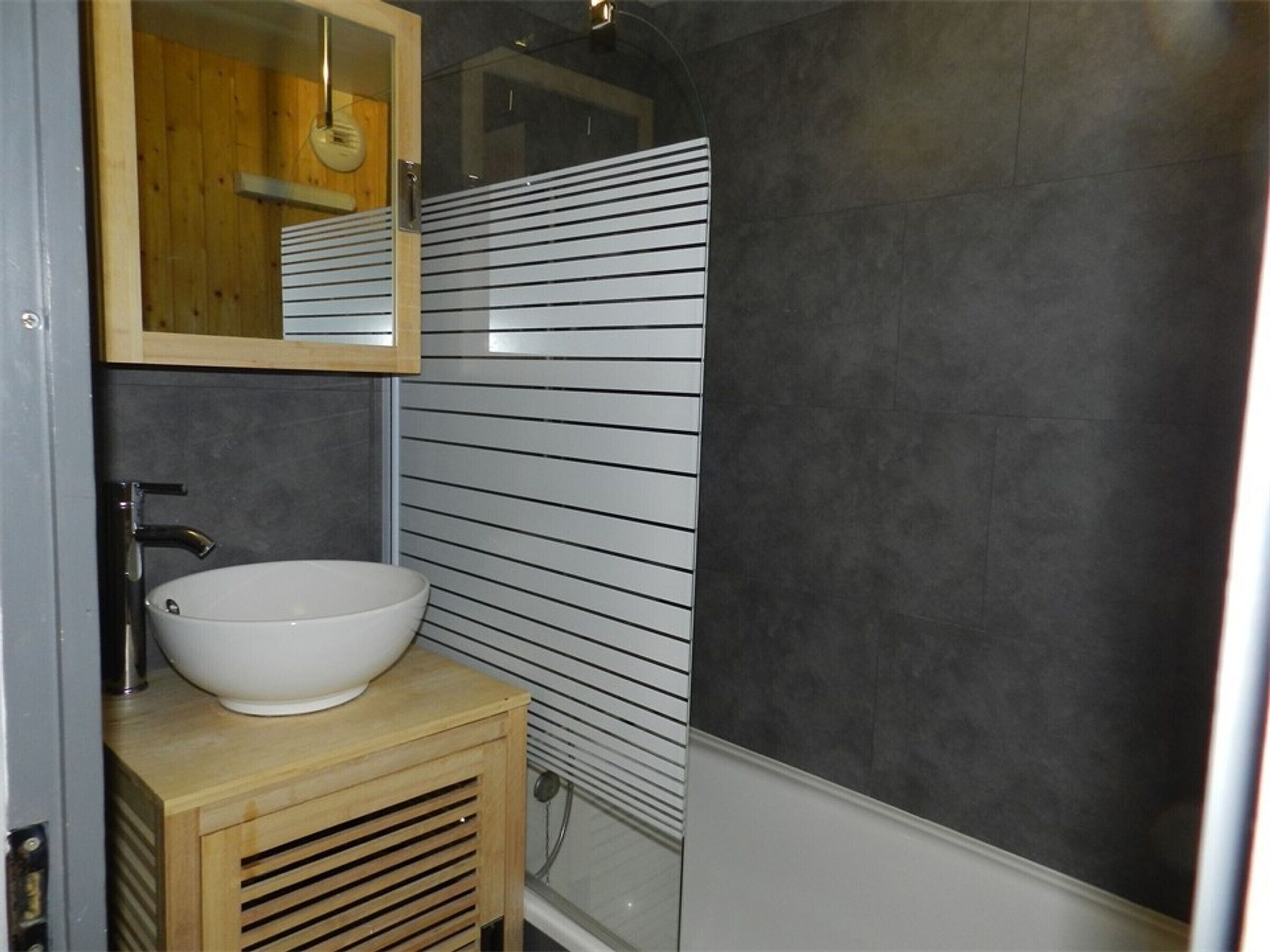 A bathroom with a wooden vanity, a white sink, and a mirror.