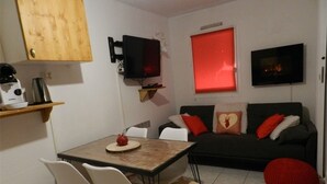 Un espacio habitable compacto con comedor, un sofá con cojines rojos y un televisor montado en la pared.