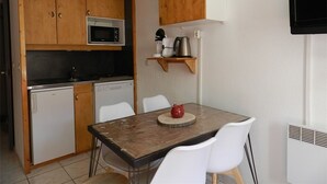 Cocina compacta con armarios de madera, microondas, cafetera y una pequeña mesa de comedor con sillas.