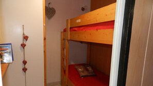 Una habitación pequeña y estrecha con una litera, un adorno de corazón en la pared y una cama individual con un osito de peluche.