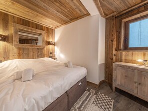 A bedroom with a wooden ceiling, a large bed, a nightstand, a dresser, and a window.
