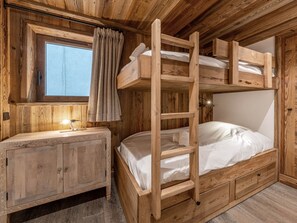 A bunk bed with a wooden ladder, a bedside table, and a window with curtains.