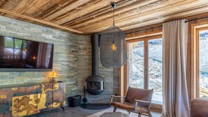 A cozy living room with a stone wall, a fireplace, a TV, and a view of the outdoors. - Luxury apartment with pool, WiFi, and parking in Val-d'Isère (Val-d'Isère)