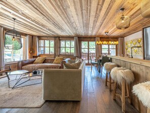A rustic interior with a wooden ceiling, leather sofas, a dining area, and a bar with stools.