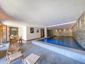A modern indoor pool area with stone walls and a ceiling with recessed lighting.