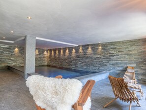 A spa area with a stone wall, a pool, and two wooden chairs.