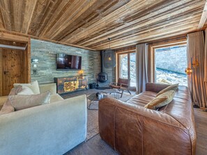 A cozy living room with a stone wall, leather sofa, and a fireplace. - Luxury apartment with pool, WiFi, and parking in Val-d'Isère (Val-d'Isère)