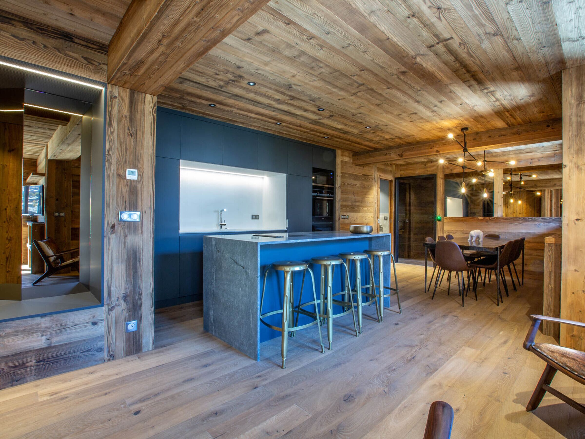 A modern kitchen with a blue countertop, wooden beams, and bar stools.
