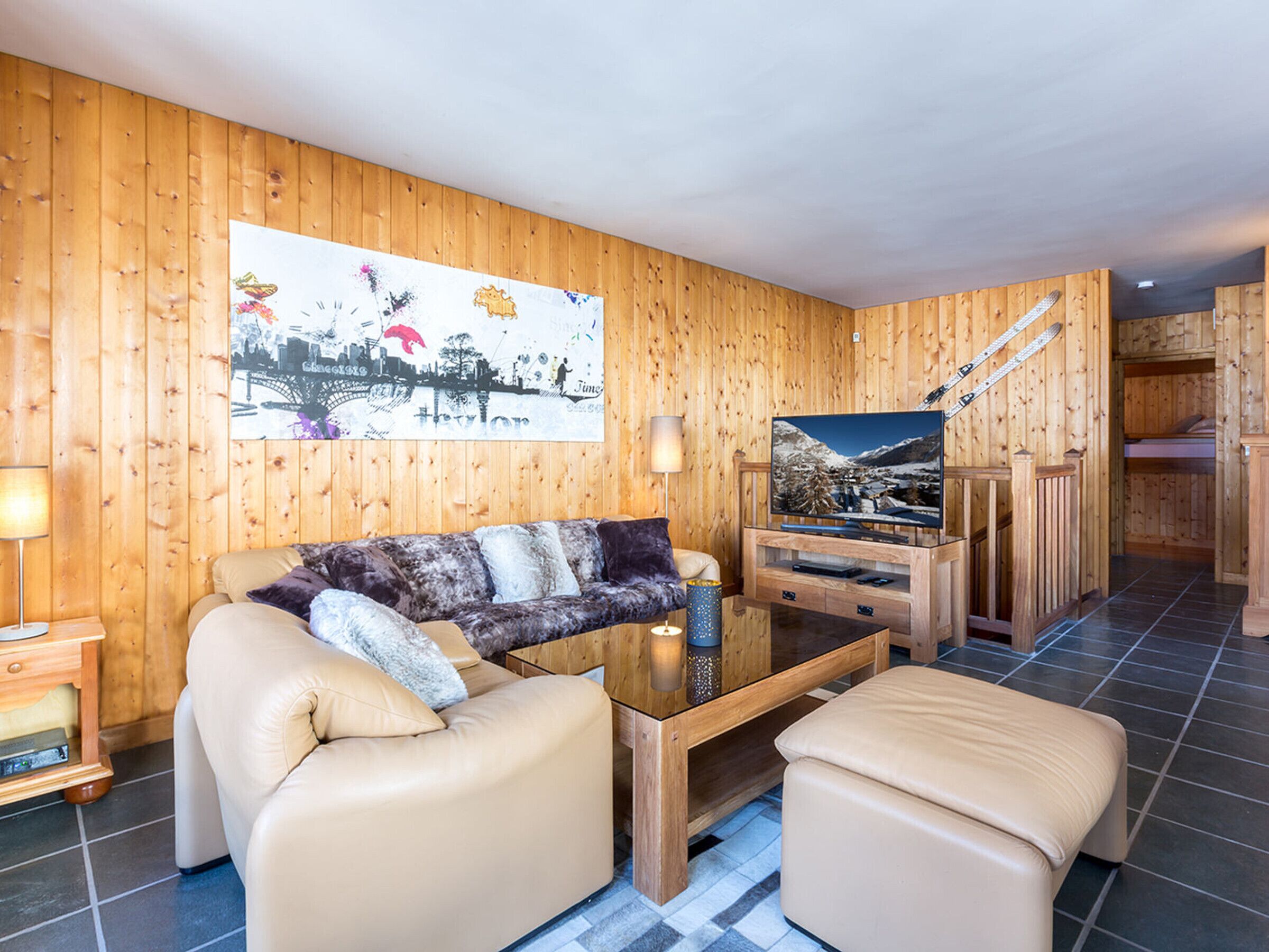 A wooden-paneled room with a sofa, ottoman, and a television on a wooden stand.
