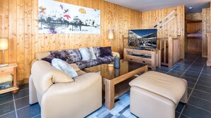 Een kamer met houten lambrisering, een bank, een voetenbankje en een televisie op een houten standaard.