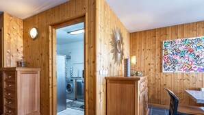 Een kamer met houten wanden, betegelde vloer, een wasmachine, een kast, een stoel en een kunstwerk aan de muur.