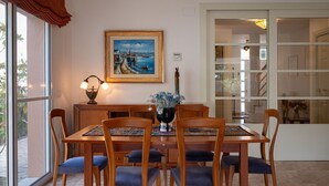 Un comedor con mesa y sillas de madera, un cuadro en la pared y vistas a través de la puerta de vidrio.