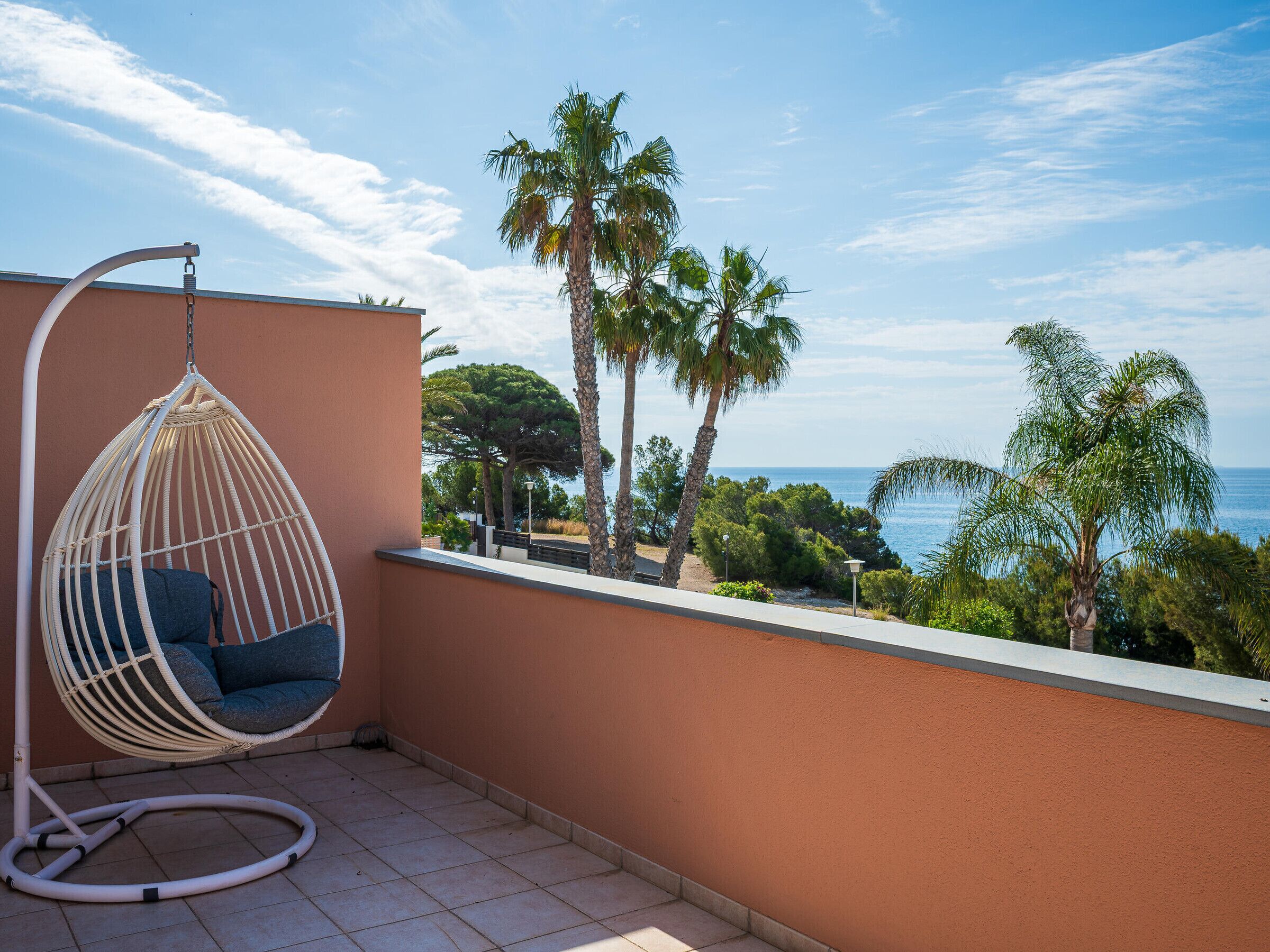 Ein Balkon mit einer Hängematte, Palmen und Blick aufs Meer.