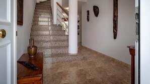 Un pasillo con una escalera de piedra, una mesa de madera con un jarrón y una puerta con picaporte de latón.