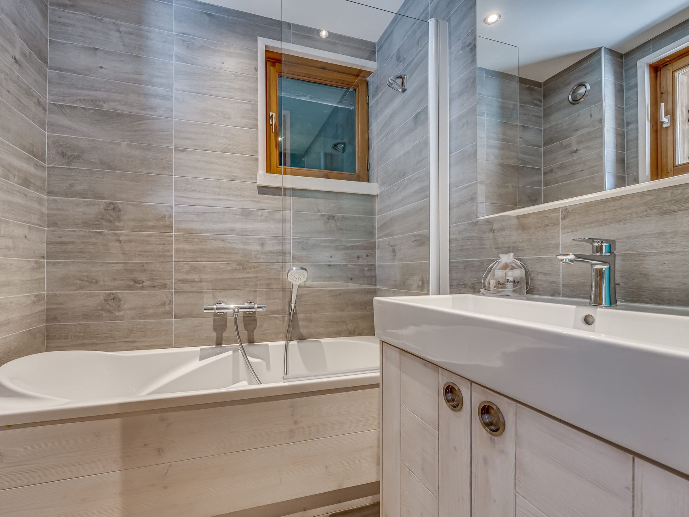 A modern bathroom with a freestanding bathtub, a large mirror, and wooden cabinetry.
