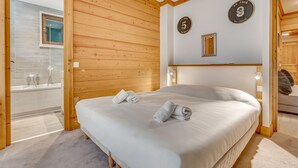 A hotel room with a wooden paneled wall, a large bed with white linens, a shower area, and a wooden ceiling.