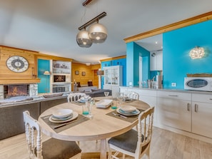 A modern kitchen with a dining area, wooden beams, a blue accent wall, and a fireplace.