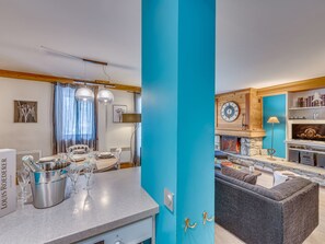 A modern kitchen with a blue accent wall, a dining area with a chandelier, and a living room with a fireplace.