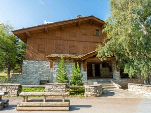 A rustic wooden building with a stone base, a wooden porch, and a stone staircase leading to the entrance.