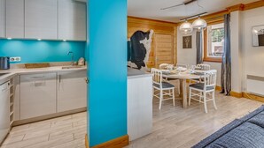 A modern kitchen with white cabinets and a blue accent wall, a dining area with white chairs and a table, and a wooden door with a cowhide decoration.
