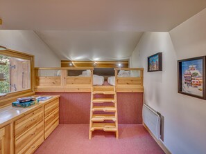 A room with bunk beds, a wooden desk, and a ladder.