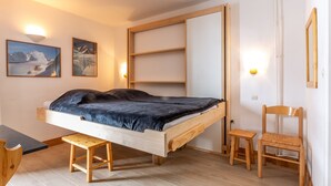Ein Zimmer mit einem Bett, einem Schreibtisch, einem Sessel und zwei Wandregalen.