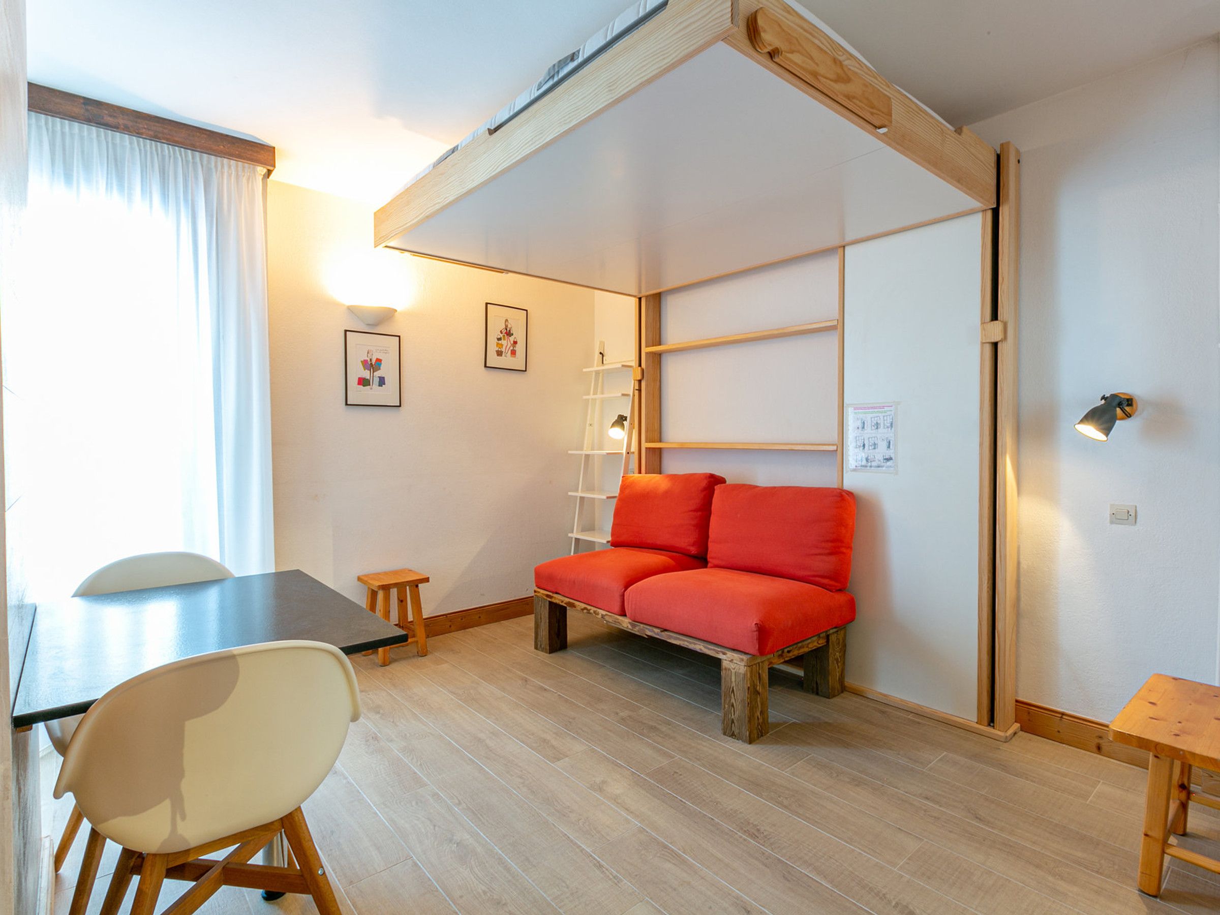 Et hyggeligt rum med en træbænk, et lille bord, en stol og en rød sofa.