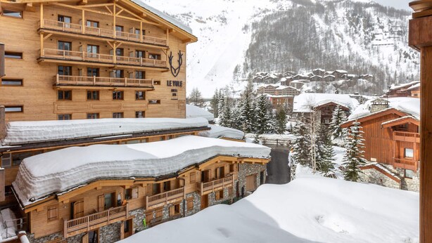 Ein Chalet-Hotel aus Holz mit mehreren Balkonen und einem Ski-Hang im Hintergrund.