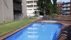 En swimmingpool med træterrasse, omgivet af et hegn og en græsplæne.