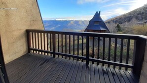 A wooden deck with a view of a mountain landscape, including a house with a pointed roof.