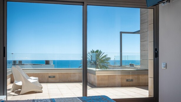 A bedroom with a large sliding glass door leading to a balcony with a view of the sea.