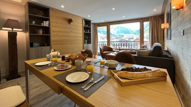 Un espace repas moderne avec une table en bois mise pour le petit-déjeuner, un canapé et une vue sur un paysage montagneux.