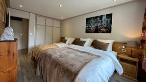 Une chambre avec deux lits, une tête de lit en bois, une table de chevet avec une lampe, un tableau représentant des cerfs et une armoire à portes coulissantes.