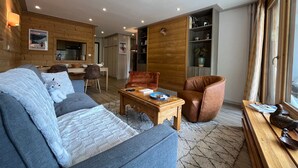 Un salon moderne avec un canapé, des fauteuils, une table basse en bois et une bibliothèque.