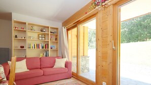 Ein gemütliches Wohnzimmer mit einem rot karierten Sofa, Holzregalen mit verschiedenen Gegenständen und einer großen Schiebeglastür, die zu einem Außenbereich führt.
