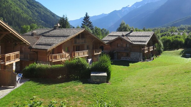 Eine Reihe von Holzhütten mit Balkonen vor einer Bergkulisse und blauem Himmel.