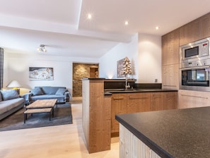 A modern kitchen with wooden cabinets, a built-in oven, and a dining area with a sofa and coffee table.