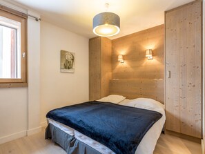 Un dormitorio con cama, cabecera de madera, ventana y lámpara fijada a la pared.