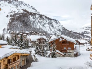 Un pueblo en la montaña cubierto de nieve, con edificios de madera, un telesilla y vistas despejadas a las montañas.