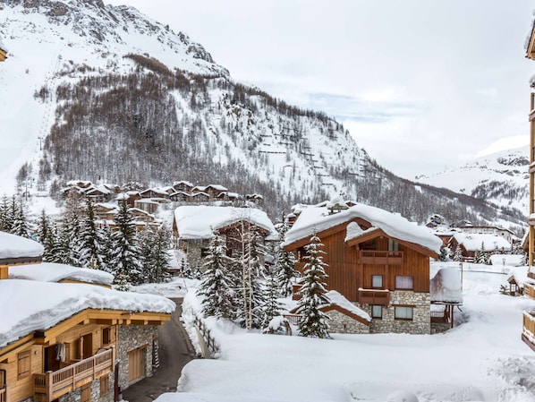 A snow-covered mountain village with wooden buildings, a ski lift, and a clear view of the mountains.