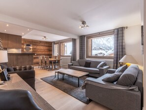 A modern living room with a sofa, a dining table, and a kitchen area with wooden paneling.