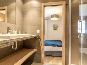 Un baño moderno con un banco de madera, un lavabo con artículos de aseo y una cabina de ducha de vidrio.